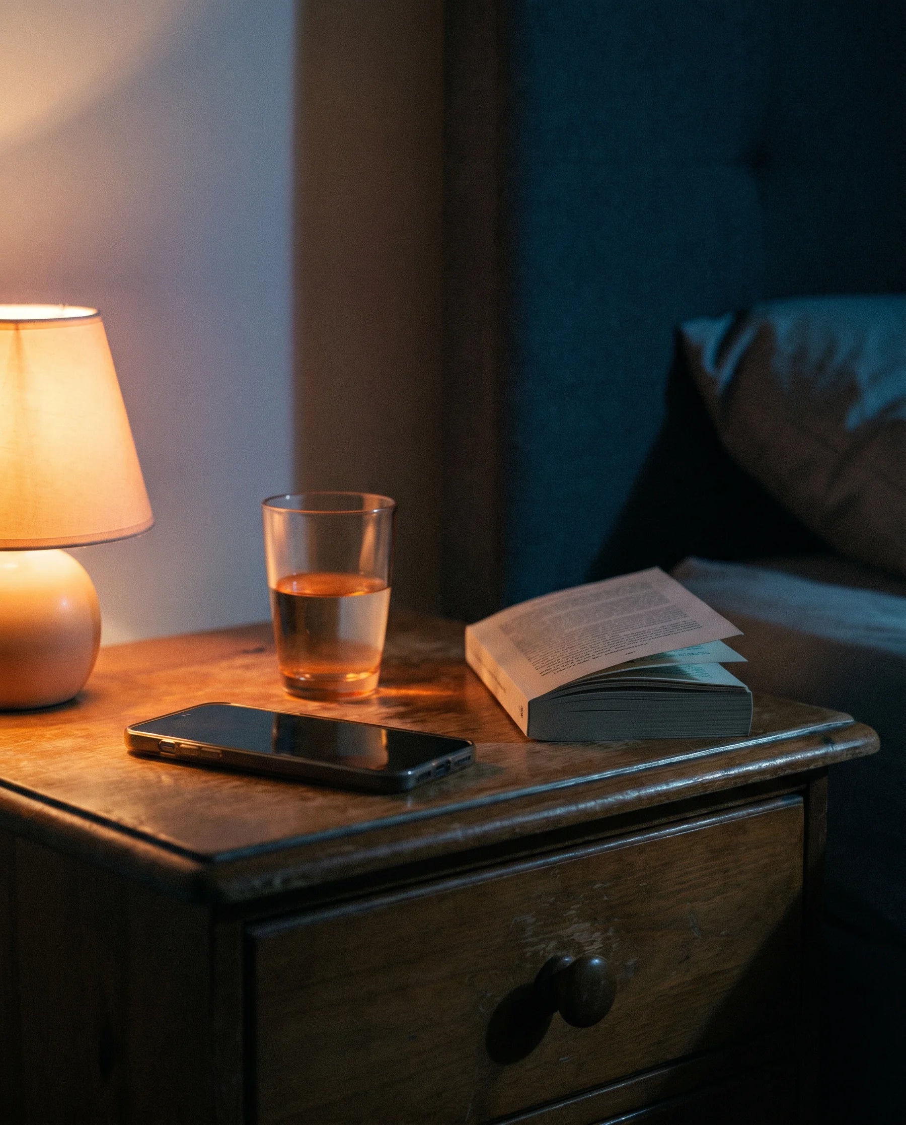 Mesa-de-cabeceira à noite: telemóvel virado para baixo, copo de água, livro fechado